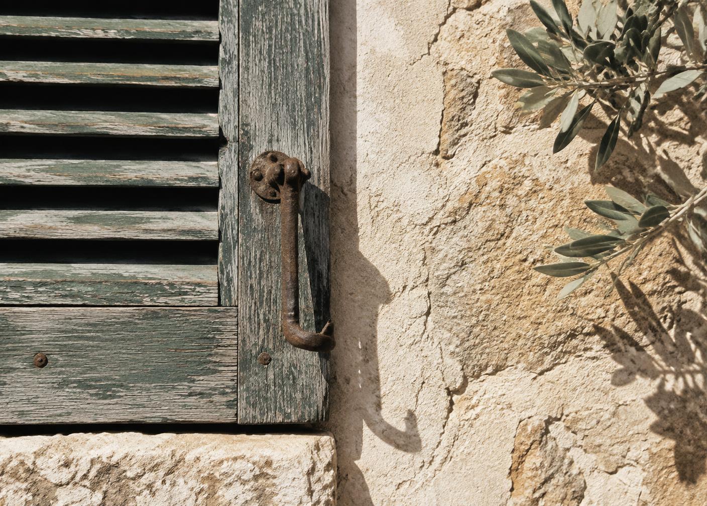 A weathered shutter and iron latch against lime plaster in hard midday sun